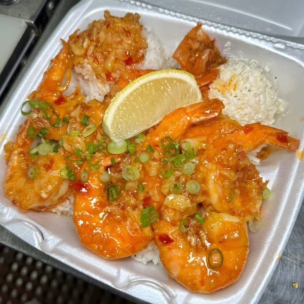 Hawaiian garlic shrimp plate with rice, macaroni salad, and a lime wedge in a takeout container.