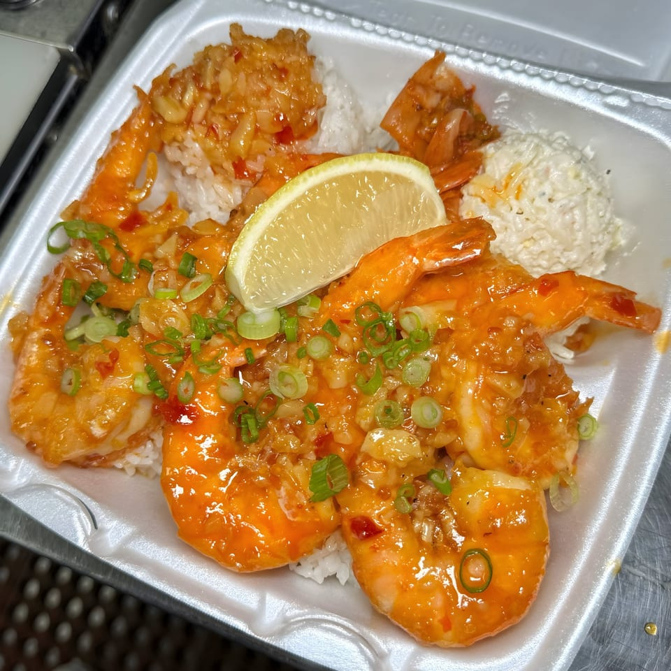 Hawaiian garlic shrimp plate with rice, macaroni salad, and a lime wedge in a takeout container.