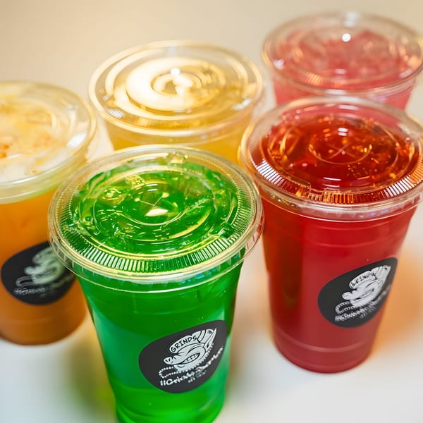 Five colorful Hawaiian drinks in clear plastic cups with Grinds 2 Da Max logos.