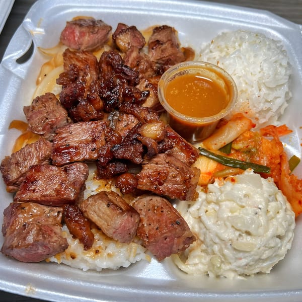 Hawaiian plate lunch with grilled steak, white rice, macaroni salad, kimchi, and a side of sauce.