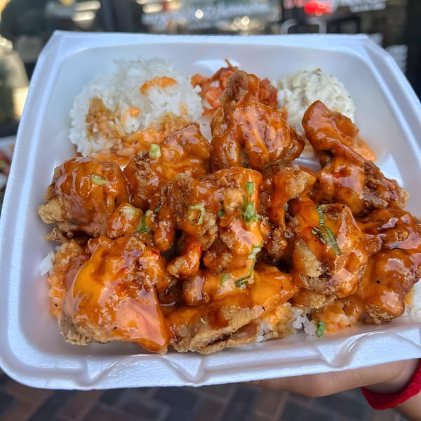 Hawaiian plate lunch with crispy orange chicken, white rice, and macaroni salad in a styrofoam container.