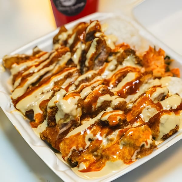 A Hawaiian plate lunch with crispy chicken, rice, and mac salad, drizzled with two sauces.